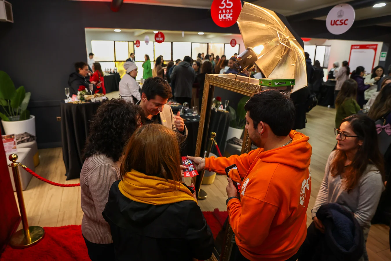 Anfitrión de Festa entrega fotografías impresas a las invitadas junto al Espejo Mágico durante un evento universitario.