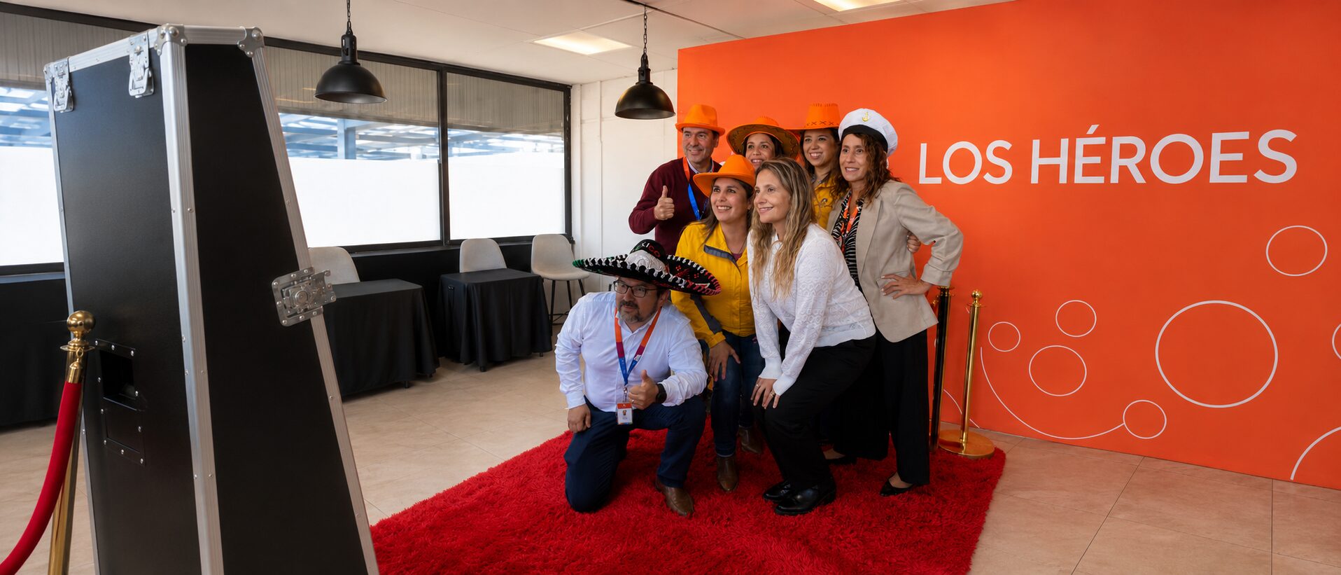 Equipo de una empresa posando con accesorios frente al Espejo Mágico de Festa sobre alfombra roja durante un evento corporativo.